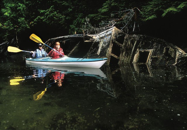 Photo of Couple kayaking past abandoned boat